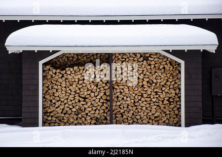 Stapel Feuerholz in einem Schuppen gestapelt. Schneebedeckte Garage gefüllt mit Holzstapeln. Stockfoto