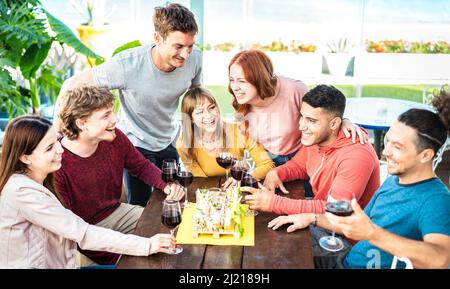 Trendige junge Leute, die sich beim Weintrinken im Penthouse im privaten Hausgarten amüsieren - glückliche Freunde, die gemeinsam in der Restaurant-Lounge Zeit genießen Stockfoto