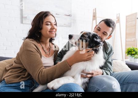 Glückliche junge Frau kuschelt australischen Schäferhund in der Nähe von Freund Stockfoto