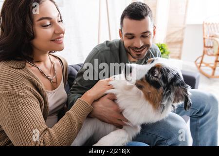 Lächelnde junge Frau kuschelt australischen Schäferhund mit glücklichen Freund Stockfoto