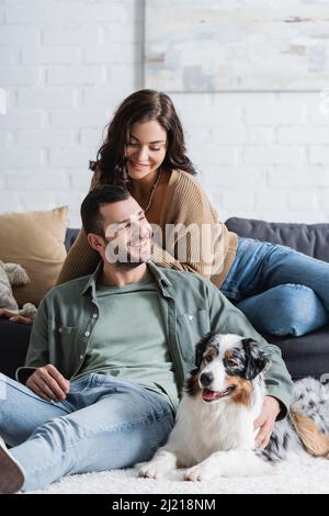 Glücklicher bärtiger Mann, der in der Nähe des australischen Schäferhundes und der brünetten Freundin sitzt Stockfoto