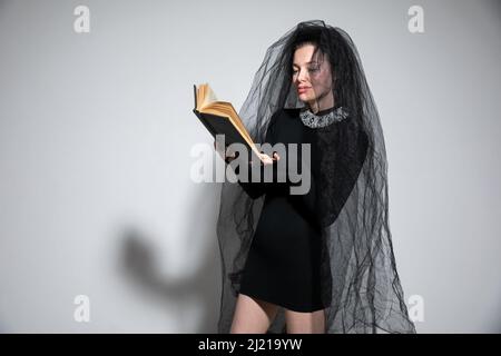 Schöne Frau in einem schwarzen Brautkleid mit einem Brautschleier und einem Buch Stockfoto