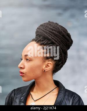 In ihrem geflochtenen Brötchen sieht es wunderschön aus. Aufnahme einer attraktiven jungen Frau mit einem geflochtenen Brötchen, das im Freien posiert. Stockfoto