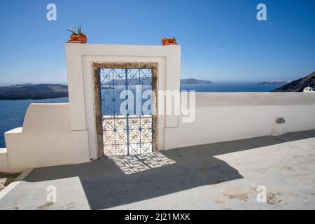 Eine außen dekorierte Tür mit Blumenpflanzen auf dem Dach einer Villa und Blick auf die Fira und die ägäis in Santorini Stockfoto