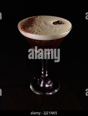 Ein schäumender Espresso martini, garniert mit Kaffeebohnen und Schokoladenstaub auf schwarzem Hintergrund Stockfoto