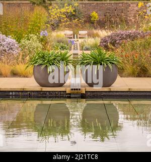 Große runde, schalenförmige Pflanzgefäße, die auf beiden Seiten der Rille platziert sind, die in den Pool im Paradise Garden auf der RHS Bridgewater mündet. Stockfoto