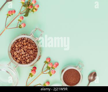 Geröstete Bio-Kaffeebohnen und gemahlener Kaffee in Gläsern mit Löffeln und Blumen auf minzem Hintergrund mit Kopierfläche. Kaffeekocher-Konzept. Entfällt Stockfoto