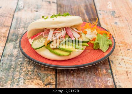 Bao-Brot-Sandwich mit Surimi, Avocado, Gurken und Schnittlauch auf einem roten Teller Stockfoto