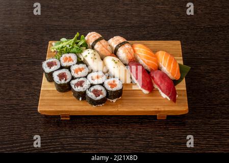 Holztablett voll mit Sushi mit rotem Thunfisch Maki und norwegischem Lachs mit Nori-Algen, Butterfisch und Garnelen-Nigiri Stockfoto