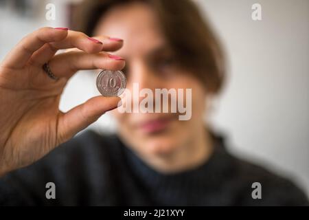 Silberbild 10 Ukrainische Hryvnia-Münze mit kyrillischen Buchstaben in der Hand einer Frau, die sie vom Hintergrund aus betrachtet Stockfoto