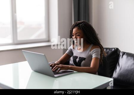 Erfolgreiche afroamerikanische junge Frau, die im modernen Büro auf dem Laptop tippt und benutzt. Geschäftskonzept Stockfoto