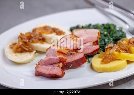 Geräucherte Flanke mit Kartoffel- und Brotknödeln und Spinat Stockfoto