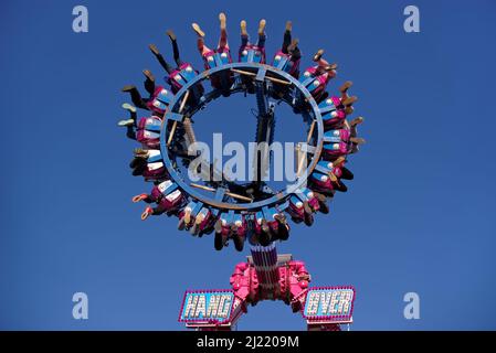 Blick auf Nervenkitzel Suchende auf dem Messegelände Fahrt gegen blauen Himmel. Drehender Ring mit den Beinen der Menschen von unten gesehen. Stockfoto