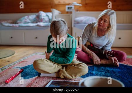 Junge mit Down-Syndrom sitzt auf dem Boden und spielt mit seiner Großmutter zu Hause Stockfoto