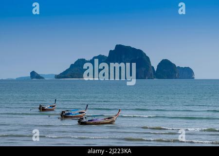 Lange Boote vertäuten vor dem Strand in Ao Nang mit Insel dahinter. Stockfoto