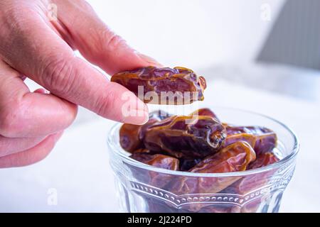 Die Hand nimmt Datteln aus der Schüssel. Traditionelles iftar-Essen für muslime. Nahaufnahme. Stockfoto