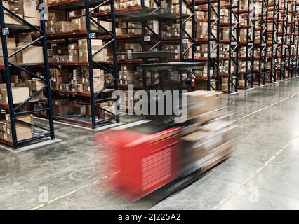 Blur eines motorisierten Stock Picker zwischen Gängen von Kartons auf Paletten auf große Racks in einem großen Distribution Warehouse gestapelt. Stockfoto