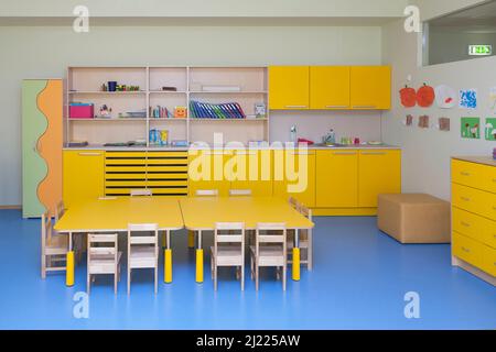 Klassenzimmer in einer Kindergartenschule, gelbe Möbel und Tische und blauer Boden. Stockfoto