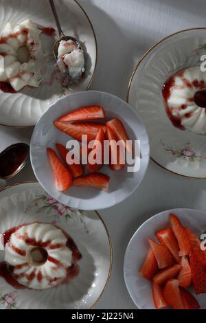 Italienische Dessert-Panna Cotta mit Obstmarmelade und frischen Erdbeerstücken auf Tellern. Draufsicht Stockfoto