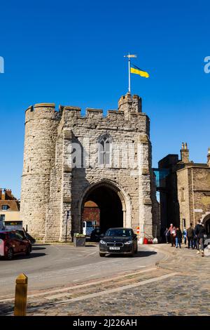 Der Verkehr fährt unter dem Bogen, Westgate Towers, Canterbury, Kent, England. Ukrainische Flagge fliegt zur Unterstützung. Stockfoto