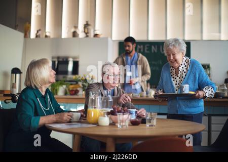Eine Gruppe von fröhlichen Senioren, die im Pflegeheim frühstücken. Stockfoto