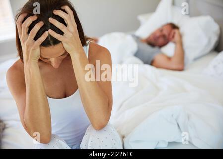 Ich habe die Nase voll von diesem ständigen Kampf. Aufnahme einer Frau, die aufgeregt aussieht, während ihr Mann im Hintergrund schläft. Stockfoto