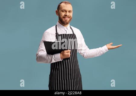 Der Kellner hält ein Menü und zeigt es mit isolierter Hand auf blauem Hintergrund Stockfoto