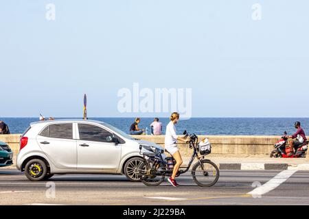 In der El Malecon Avenue kann man einen jungen Menschen beobachten, wie er mit einem Elektrofahrrad oder E-Bike fährt. Andere Transportfahrzeuge sind an der berühmten Ufermauer zu sehen. Stockfoto