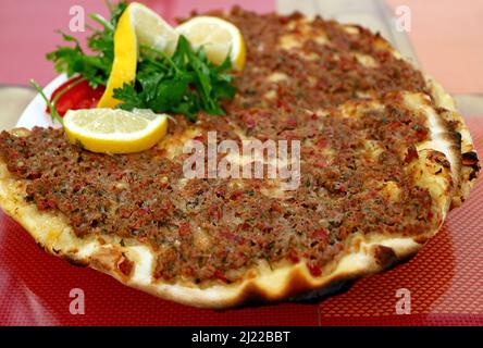Teller mit Lahmacun, einer dünnen und knusprigen türkischen Pizza, gekrönt mit gewürztem Hackfleisch Stockfoto