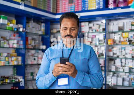 Apotheker beschäftigt mit Mobiltelefon im Einzelhandel Pharma Medical Store - Konzept der Entspannung, Überprüfung der Bestände und kleine Unternehmen. Stockfoto