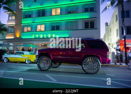 Avalon Hotel im Art déco-Stil am Ocean Drive in Miami at Dusk mit einem Oldtimer vor dem Hotel und einem GMC-SUV, der mit Big Wheels vorbeifährt Stockfoto