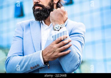 Geschäftsmann zeigt auf seine Uhr im Hintergrund der Stadt. Der Mann hält seine Uhr. Porträtieren Sie erfolgreiche Geschäftsmann in einem Geschäftsanzug mit dem Stockfoto