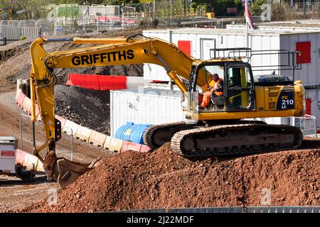 Taffs Well, Wales - März 2022: Person, die als großer mechanischer Bagger auf einem großen Haufen Schotter arbeitet. Stockfoto