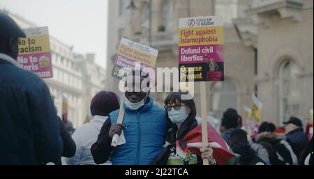 London, Großbritannien - 03 19 2022: Schwarzer Mann und schwarze Frau, die beim Fotografieren Zeichen halten, ‘Stand Up to Racism…’, am Portland Place. Stockfoto