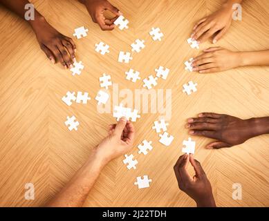 Bald wird alles Sinn machen. Eine kurze Aufnahme einer Gruppe von Geschäftsleuten, die zusammen ein Puzzle auf einem Tisch fertig stellen. Stockfoto