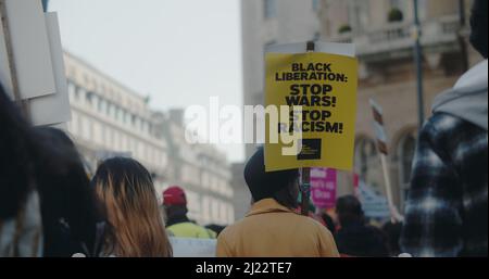 London, Großbritannien - 03 19 2022: Protesterin in Menschenmenge mit einem Schild am Portland Place, ‘Black Liberation: Stop Wars! Stoppen Sie Rassismus!“. Stockfoto