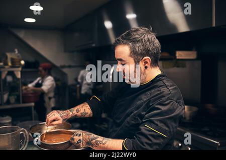 Alles für den Kurs vorbereiten. Aufnahme eines fokussierten Küchenchefs, der in der Küche eines Restaurants ein Gericht zubereitet. Stockfoto