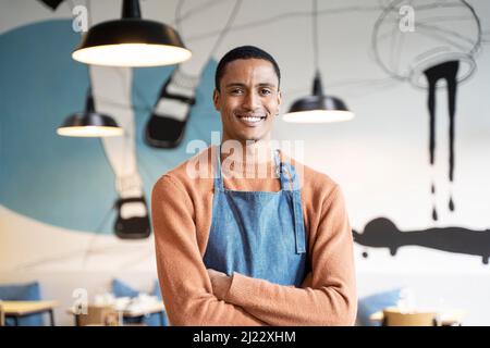 Lächelnder Besitzer oder Kellner in Arbeitsuniform stehen in moderner Cafeteria oder Restaurant Pub - Stellenangebot Konzept - Arbeiten in Catering Stockfoto