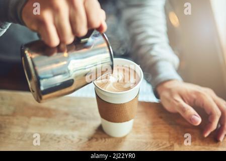 Eine perfekte Mischung kommt gleich. Nahaufnahme eines unerkennbaren Barista, der in einem Café Milch in eine Tasse frisch gebrühten Kaffee gießt. Stockfoto