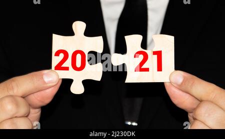 Mann stellt Holzpuzzles 2021. Das Konzept des Beginns des neuen Jahres. Neue Ziele. Nächstes Jahrzehnt. Trends und Veränderungen in der Welt. Erstellen von Plänen und p Stockfoto