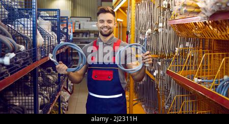 Porträt eines glücklichen Verkäufers im Baumarkt, der im Gang steht, Schläuche hält und lächelt Stockfoto