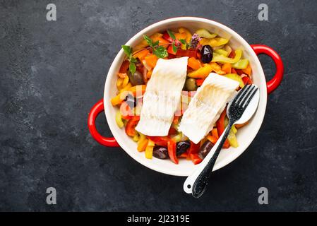 Kabeljaufilet. Im Ofen gebackener weißer Fisch auf einem Gemüsekissen. Tomaten, Paprika, Zitrone, Oliven und Fisch. Draufsicht. Stockfoto