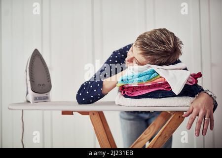 Hausarbeit ist hektisch. Aufnahme einer Frau mit dem Kopf nach unten auf einem Stapel Kleidung auf einem Bügelbrett. Stockfoto