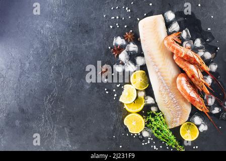 Kabeljau Garnelen Hintergrund. Weißes Fischfilet, gefrorene Garnelen auf dunklem Grund mit Zitrone, Eis, Anise und Thymian. Hintergrund für Ihre Seiten Stockfoto