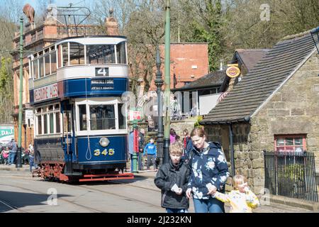 Derbyshire, Großbritannien – 5. April 2018: Familie überquert die Strecke vor der Doppeldecker-Oldtimer-Straßenbahn 345 an der Straßenbahnhaltestelle Red Lion, Crich Tramway Village Stockfoto