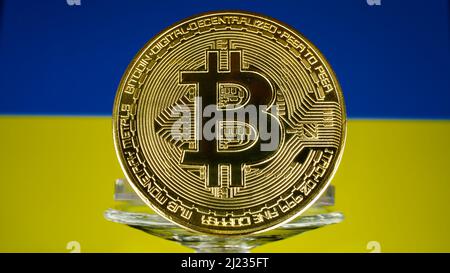 Golden Kryptowährung Bitcoin vor der Flagge der Ukraine. Der Fokus liegt auf der Münze vorne. Stockfoto