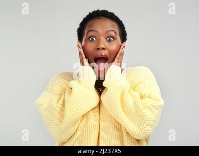 Ich kann meinen Augen nicht glauben. Aufnahme einer jungen Frau, die überrascht vor grauem Hintergrund posiert. Stockfoto