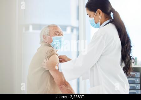 Es wird vorbei sein, bevor Sie es wissen. Aufnahme einer Ärztin mit Gesichtsmaske und Vorbereitung ihrer älteren Patientin auf einen Covid-Impfstoff in ihrer Klinik. Stockfoto