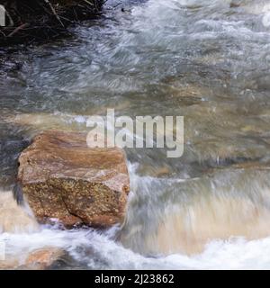 Schöner Naturstein sitzt isoliert gegen das fließende Wasser eines Baches oder Baches Stockfoto