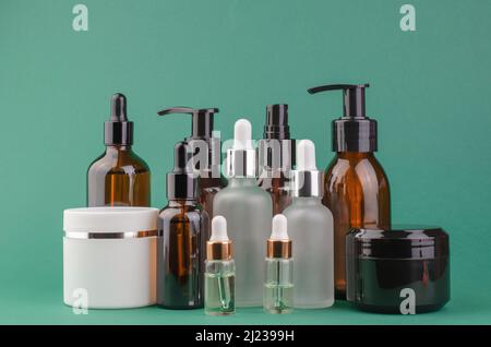 Kosmetikflaschen verschiedener Art und Gläser für Creme auf grünem Hintergrund Stockfoto